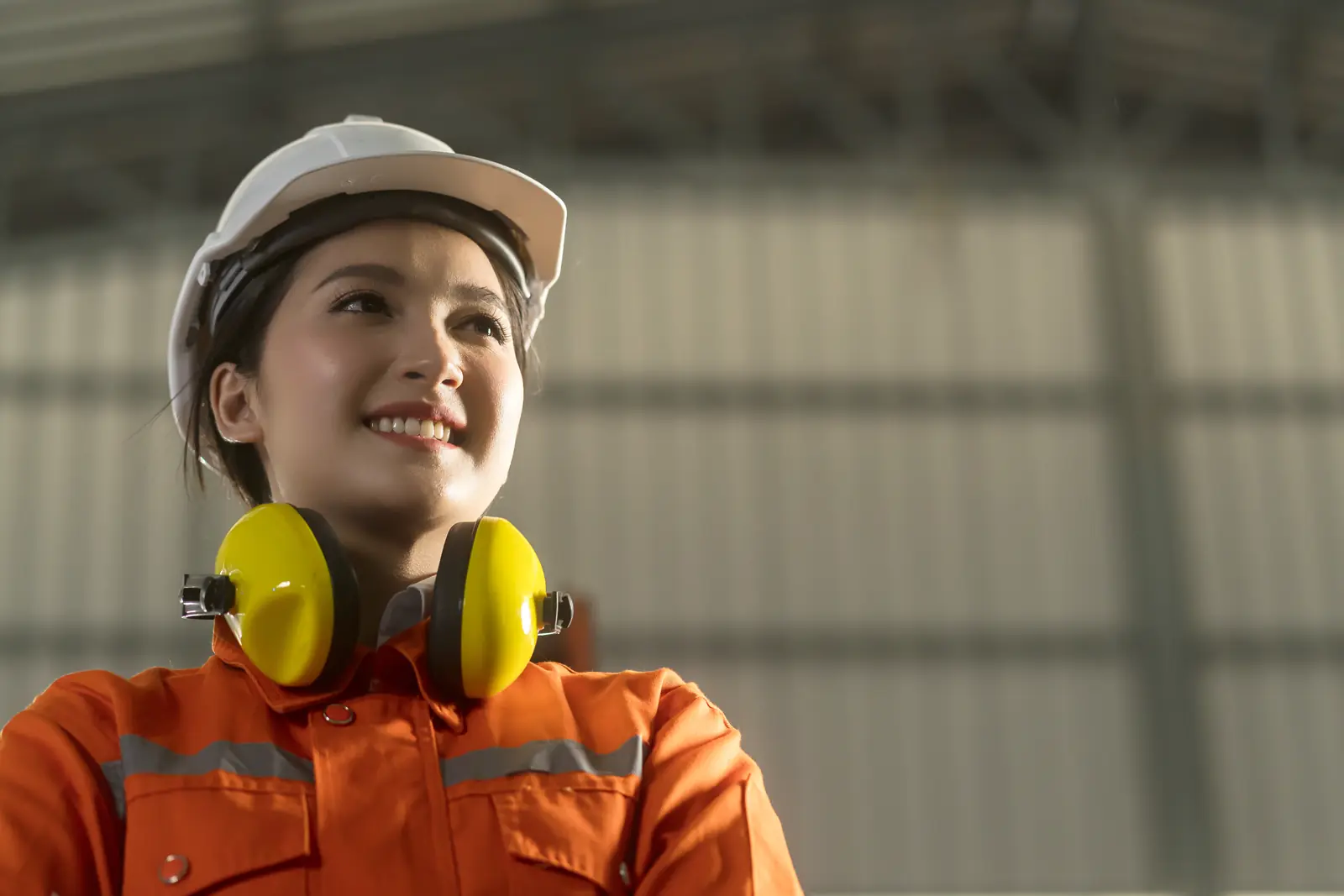 Operaria con casco de seguridad y protectores auditivos en planta industrial, usando EPP de seguridad ocupacional